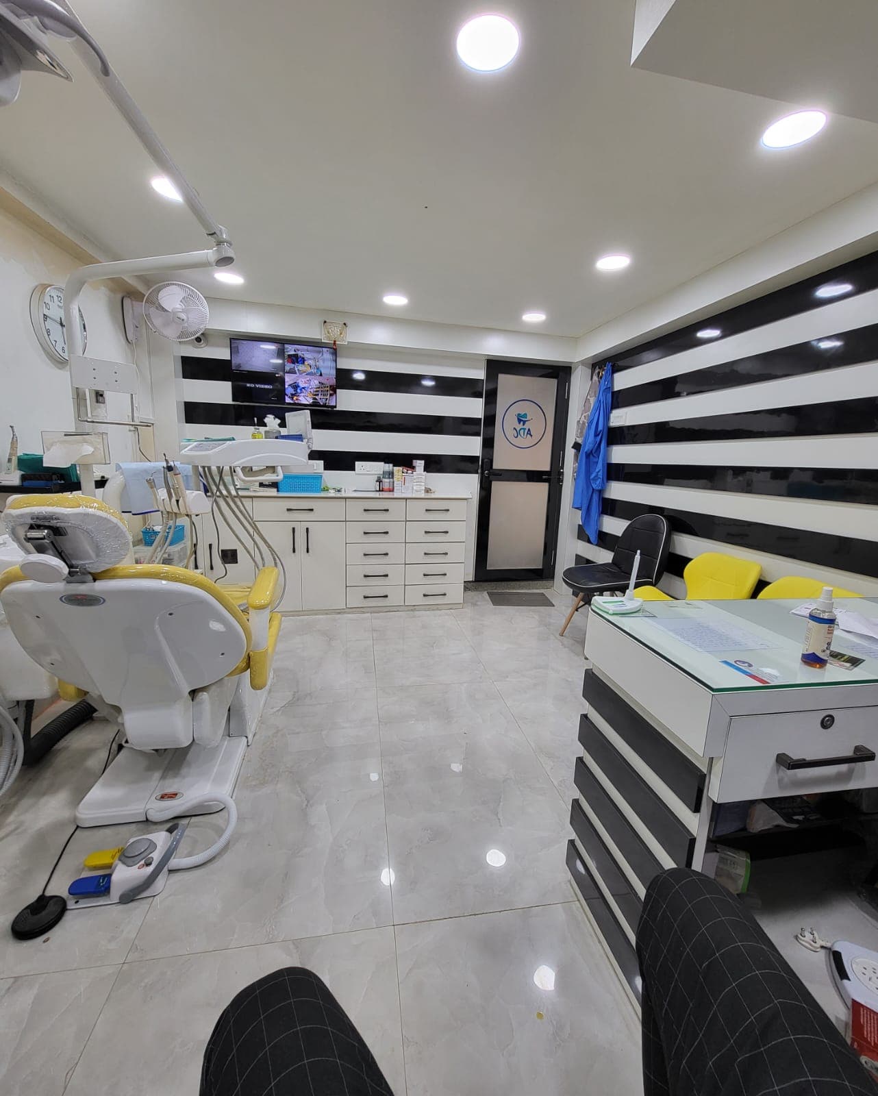 Modern dental clinic with a yellow chair, black and white striped walls, and white cabinetry.