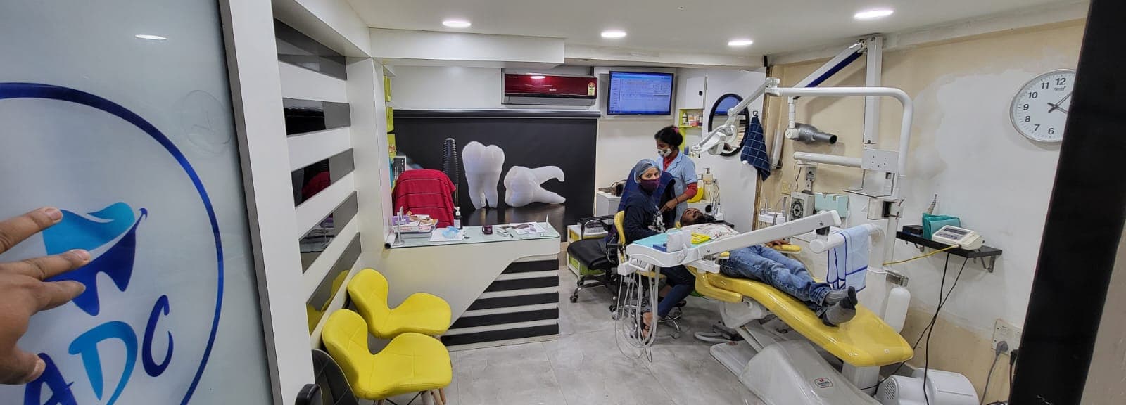Patient receiving treatment in a yellow dental chair within a modern, well-equipped dental clinic.