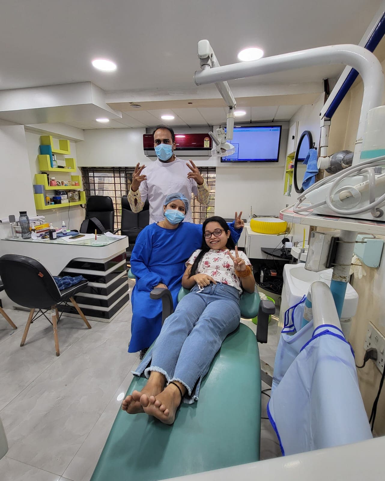 Smiling patient and two dental professionals making peace signs inside a bright dental clinic.