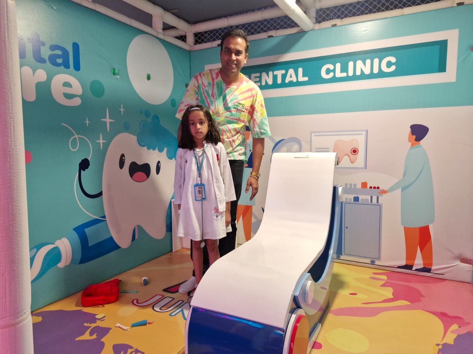 Man and girl in a dentist costume posing in a colorful play dental clinic.