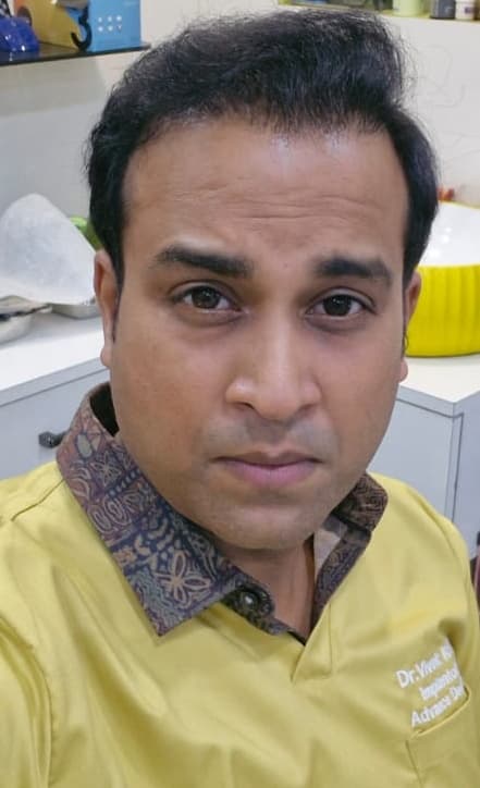 A man with dark hair wearing a yellow shirt with a patterned collar looking forward.
