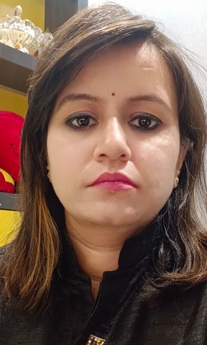 Woman with brown hair, a bindi, and pink lipstick wearing a black collared top.